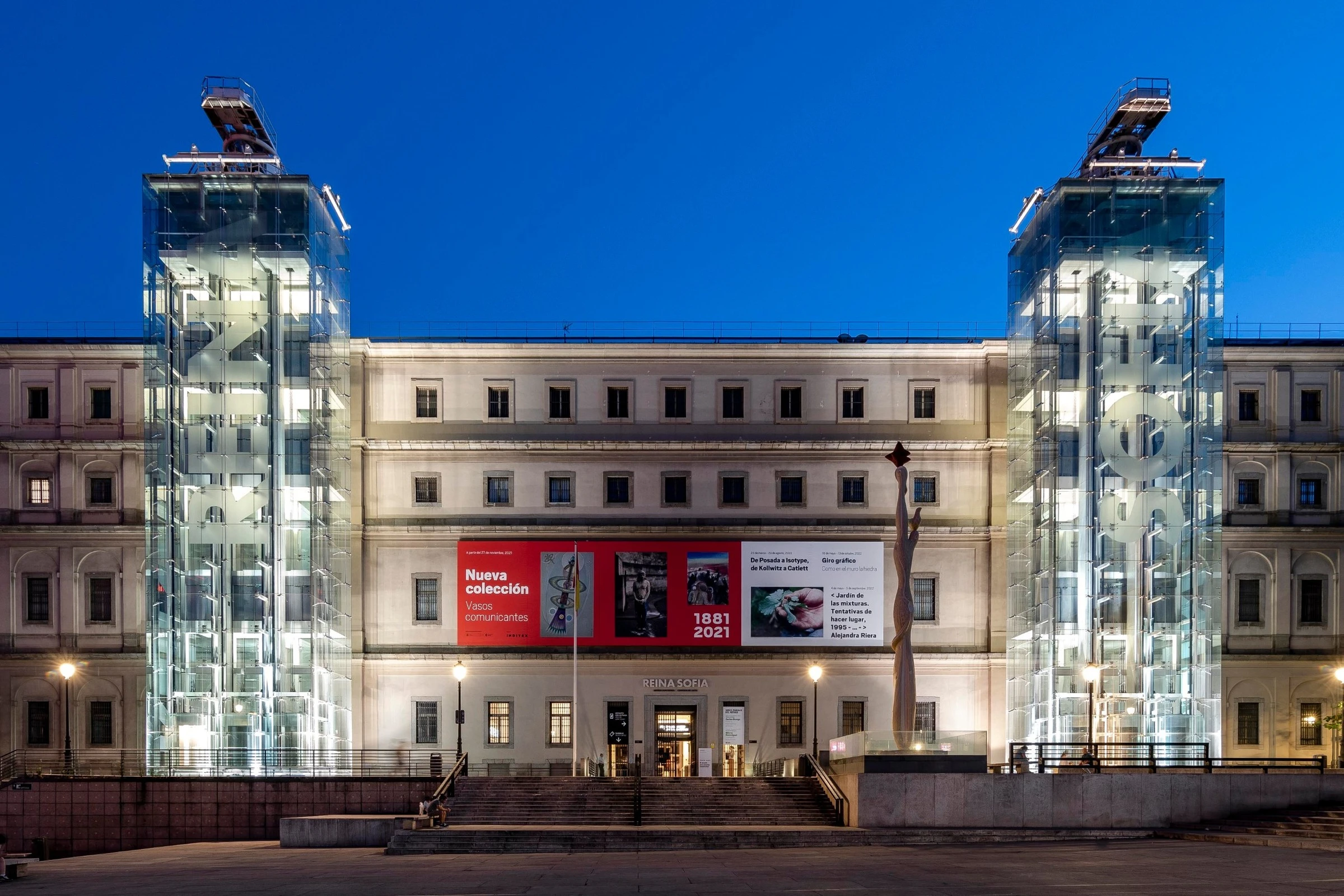 The glass towers of the Reina Sofía Museum lit up against a deep blue evening sky.