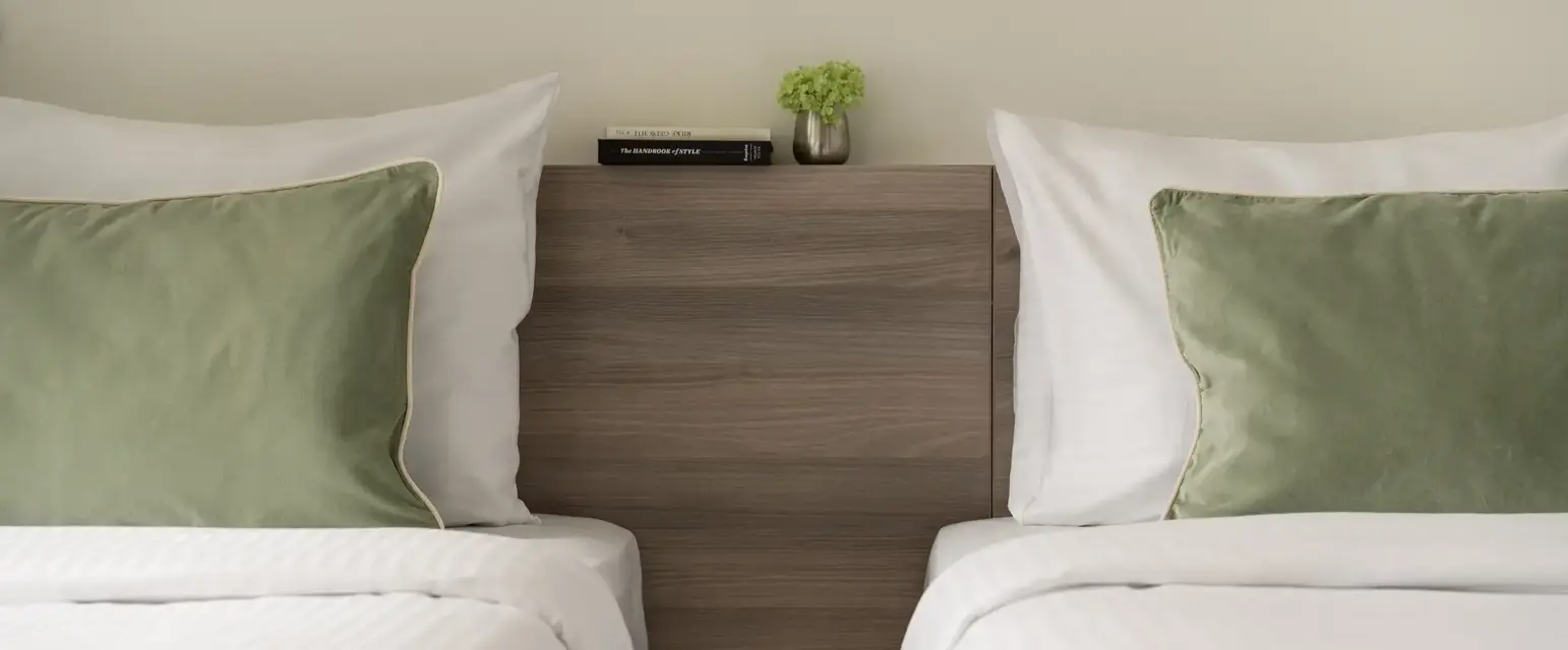 two beds with pillows and a vase of flowers on top of them