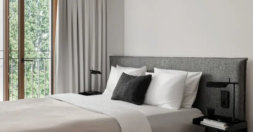 a bed with a black pillow and a table next to a window