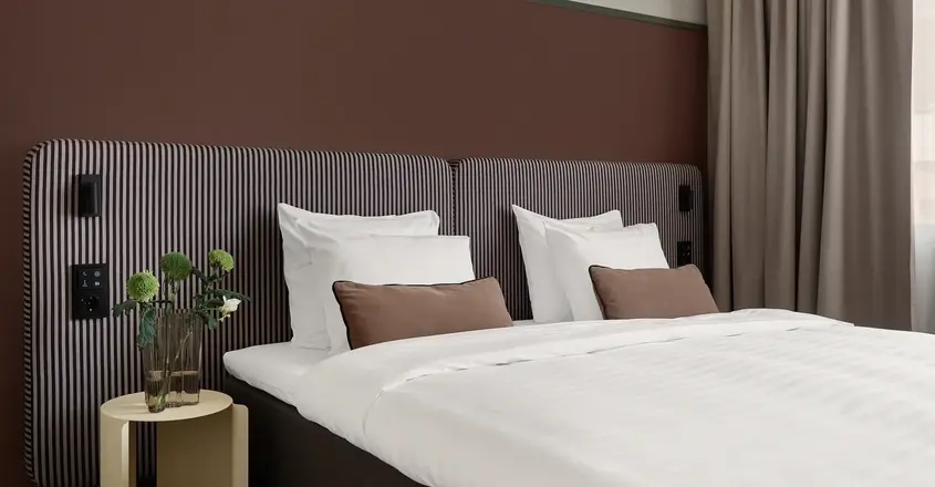 a bed with white sheets and brown striped headboard