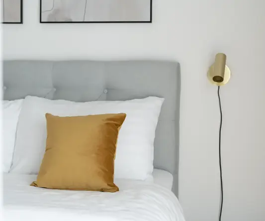 a bed with a gold pillow and a lamp on the wall