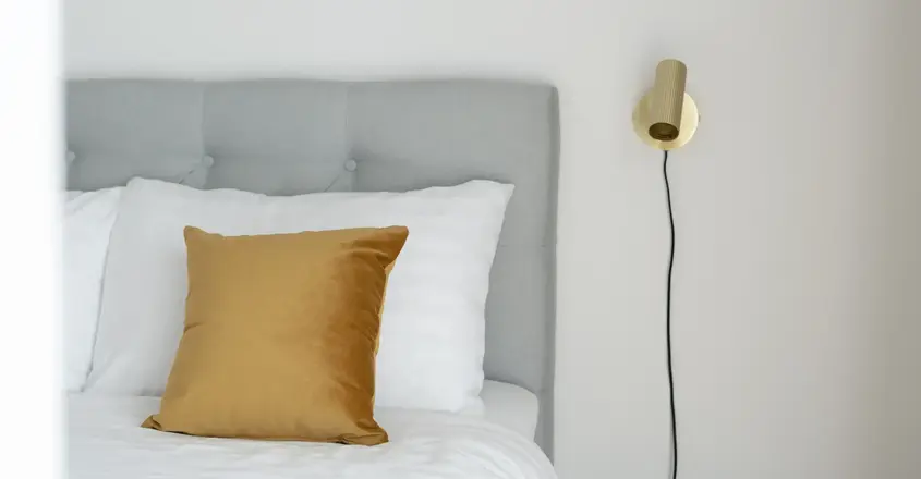 a bed with a gold pillow and a lamp on the wall