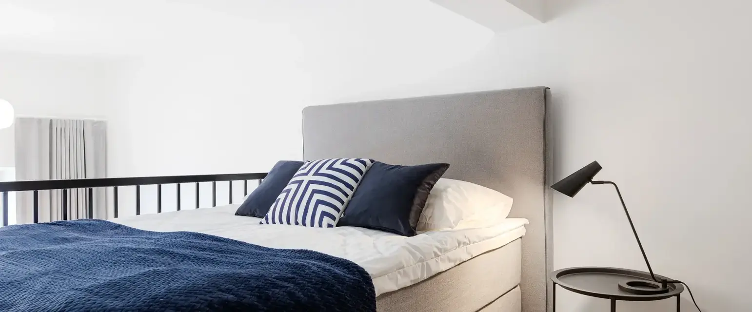 a bed with a blue blanket and a black lamp