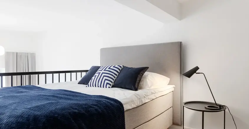 a bed with a blue blanket and a black lamp