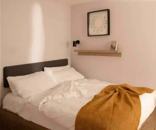 a bed with white sheets and orange blanket