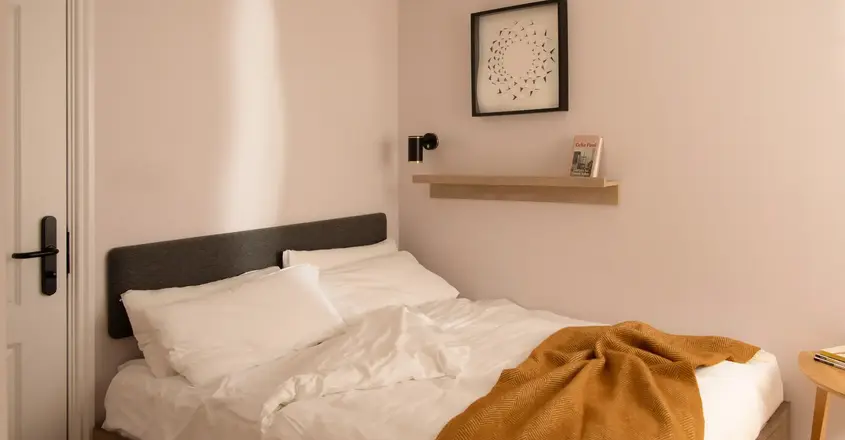 a bed with white sheets and orange blanket