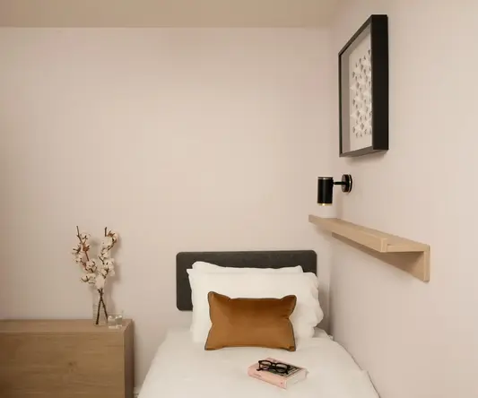 a small bed with a book and a brown pillow