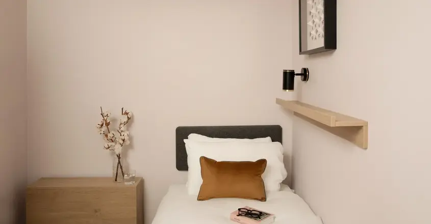 a small bed with a book and a brown pillow
