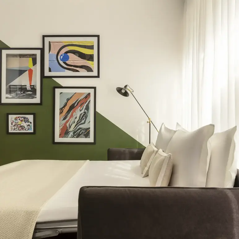 a bed with white pillows and a green wall with pictures on the wall