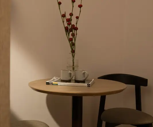a table with a vase of red flowers and two mugs on it