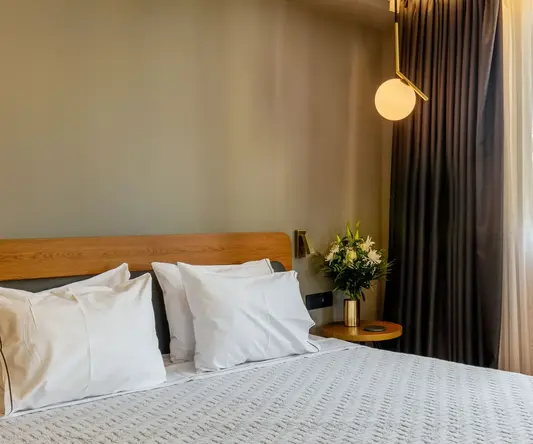 a bed with white pillows and a vase of flowers in front of a window