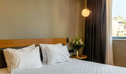 a bed with white pillows and a vase of flowers in front of a window