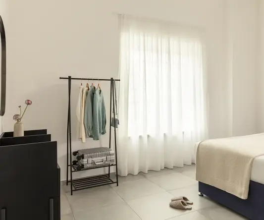 a room with a bed and a rack with clothes and shoes