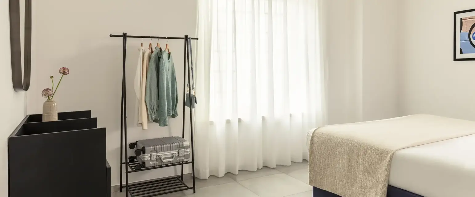 a room with a bed and a rack with clothes and shoes