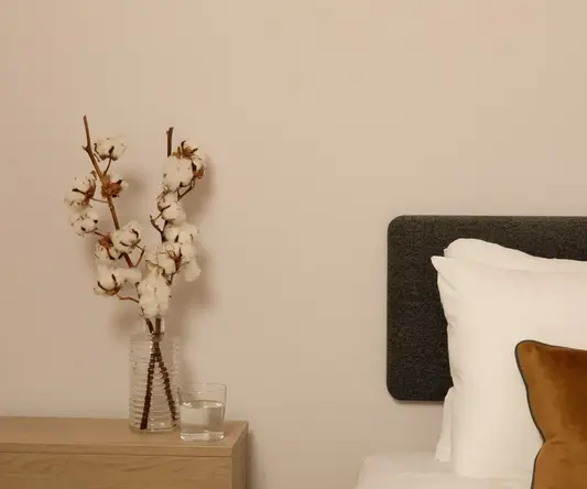 a vase of cotton flowers on a table next to a bed