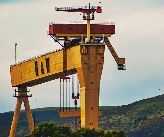 a large yellow crane with a large green hill behind it