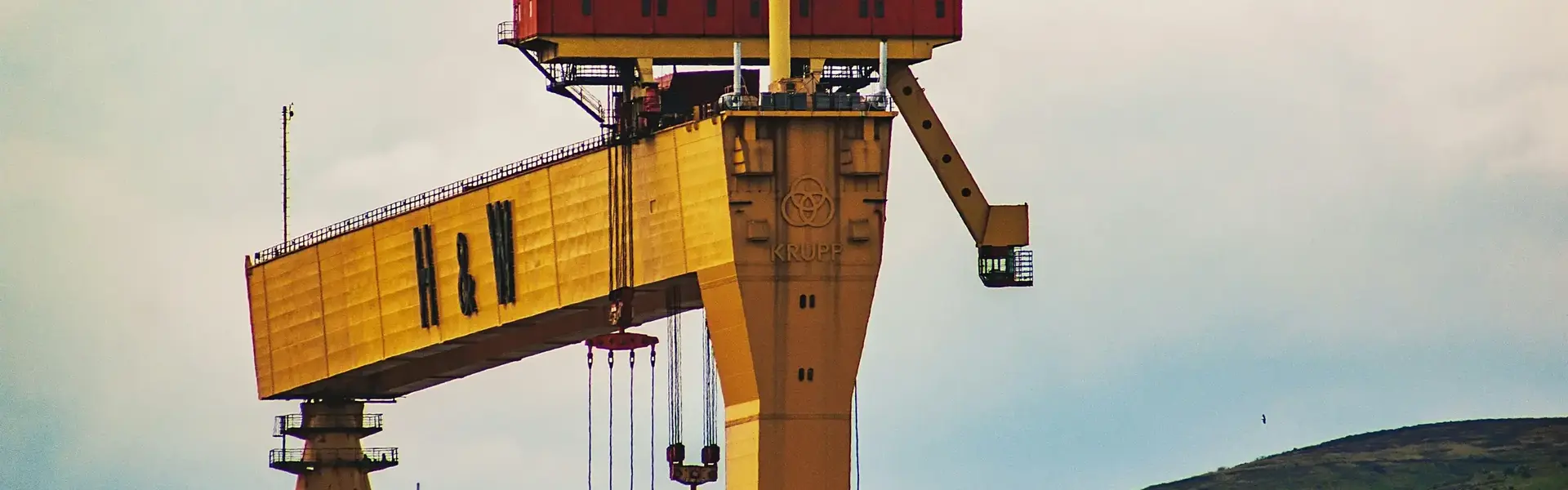 a large yellow crane with a large green hill behind it