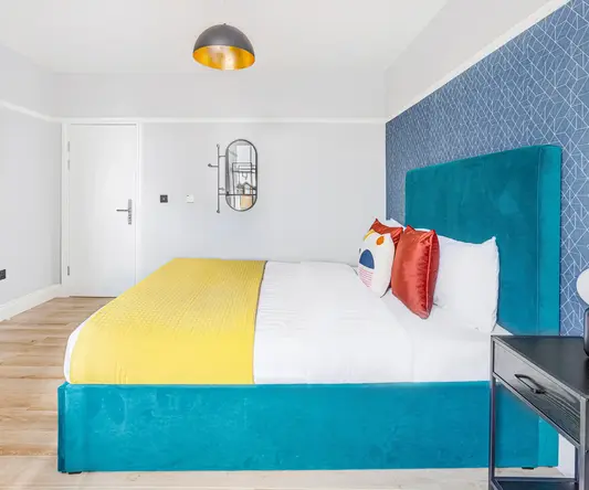 a bed with a blue headboard and yellow and red pillows