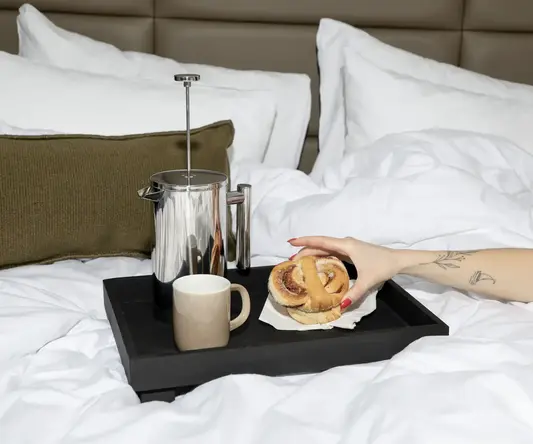 a hand holding a pastry on a tray with a coffee cup and a mug