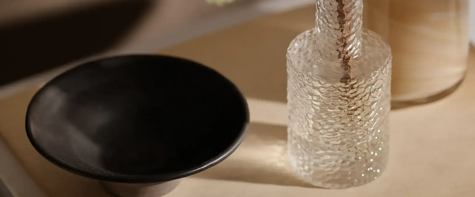 a glass vase with a stem in it and a candle on a table