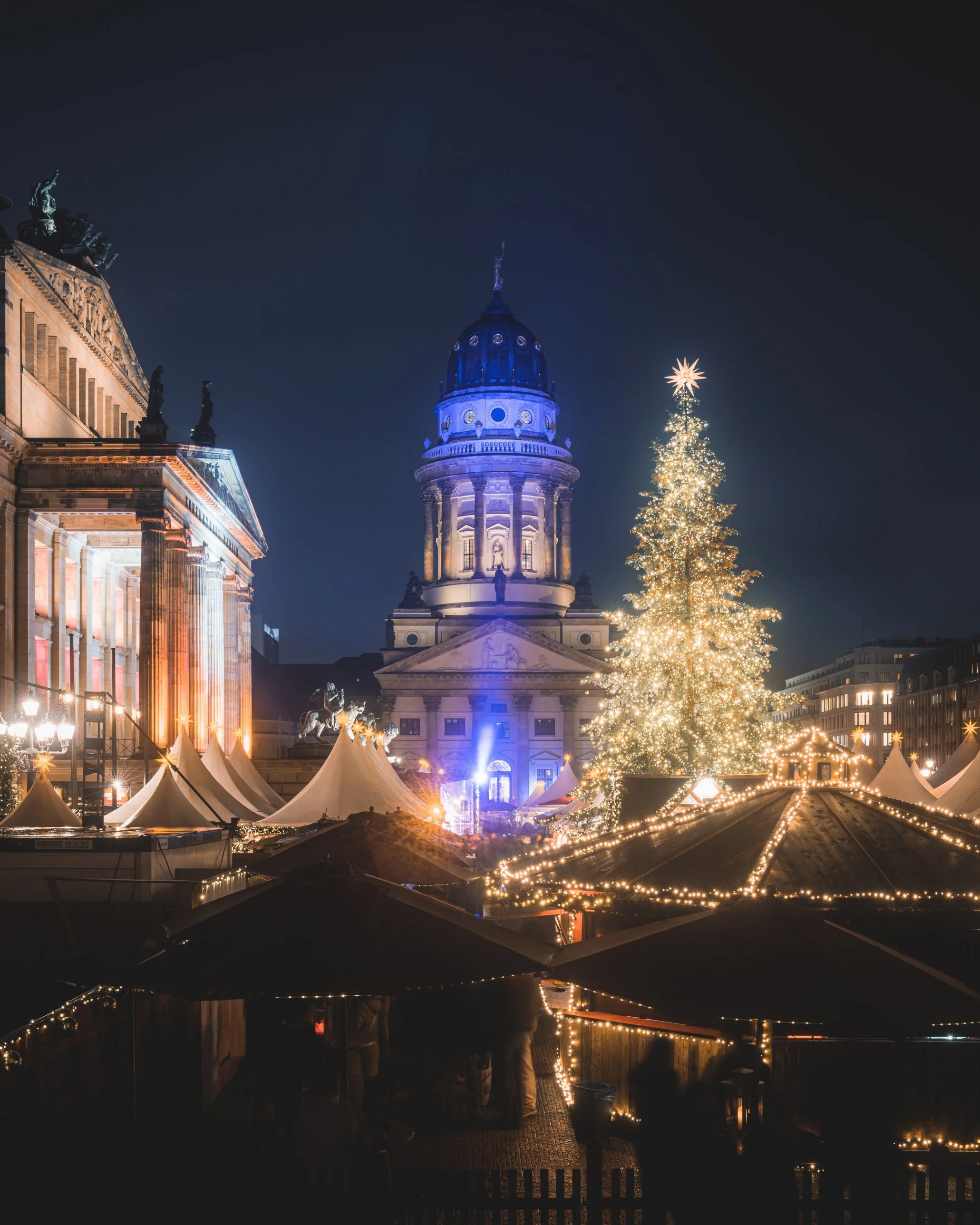 The French Cathedral lit blue beside a tall golden Christmas tree at the Gendarmenmarkt market