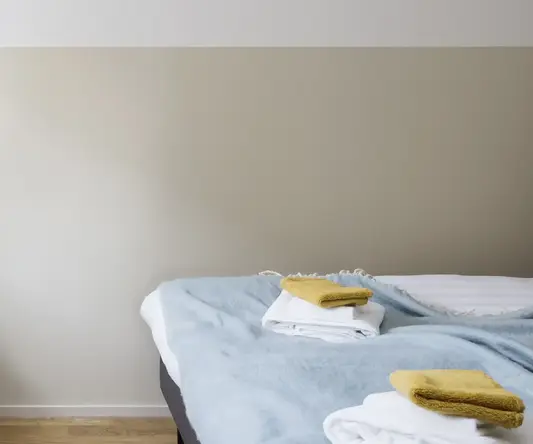 a bed with a blue blanket and a white vase on a table