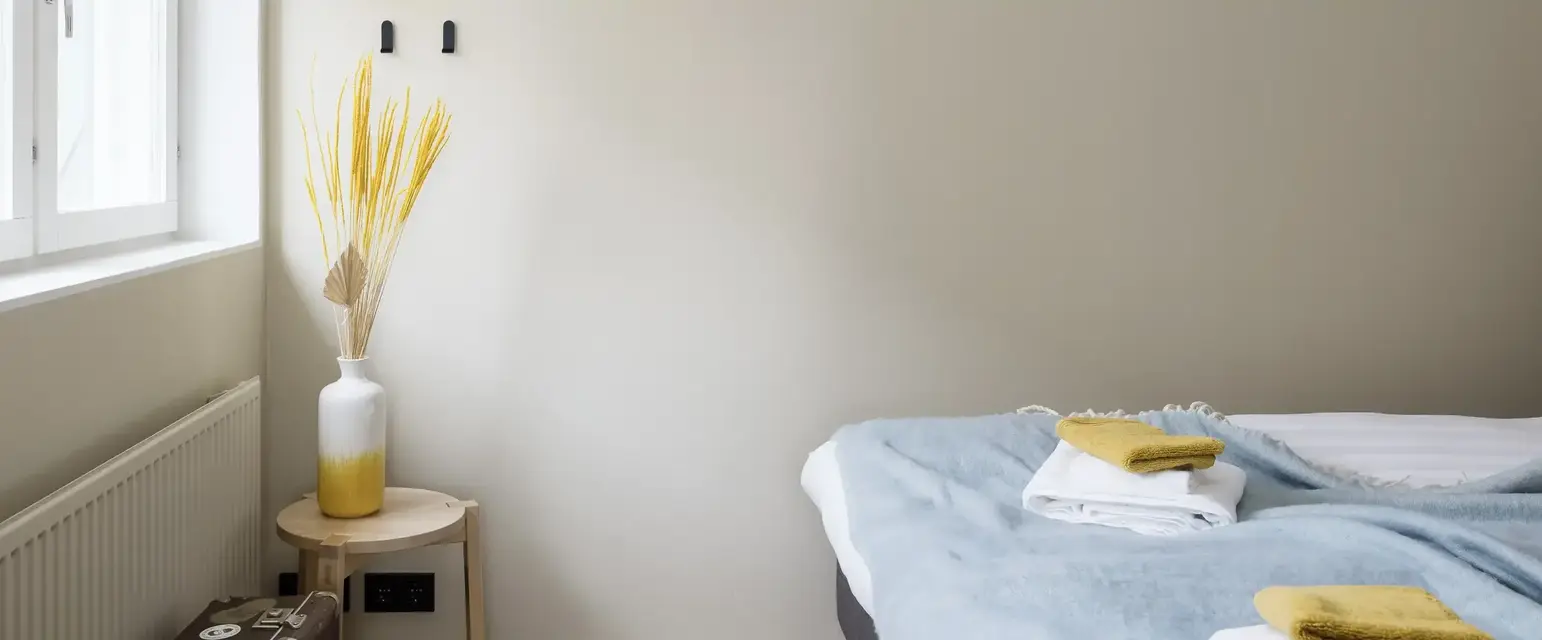 a bed with a blue blanket and a white vase on a table