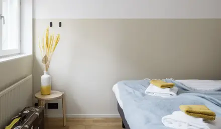 a bed with a blue blanket and a white vase on a table