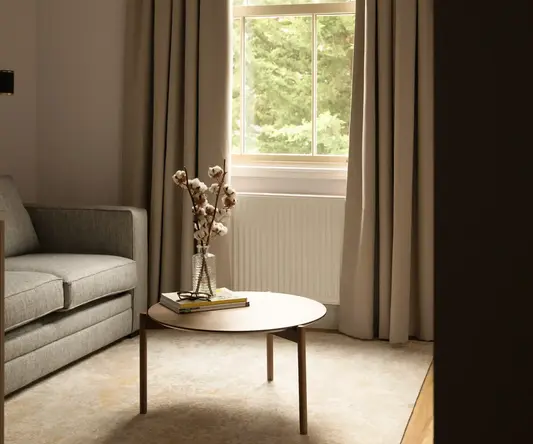 a table with a vase of cotton flowers in front of a window