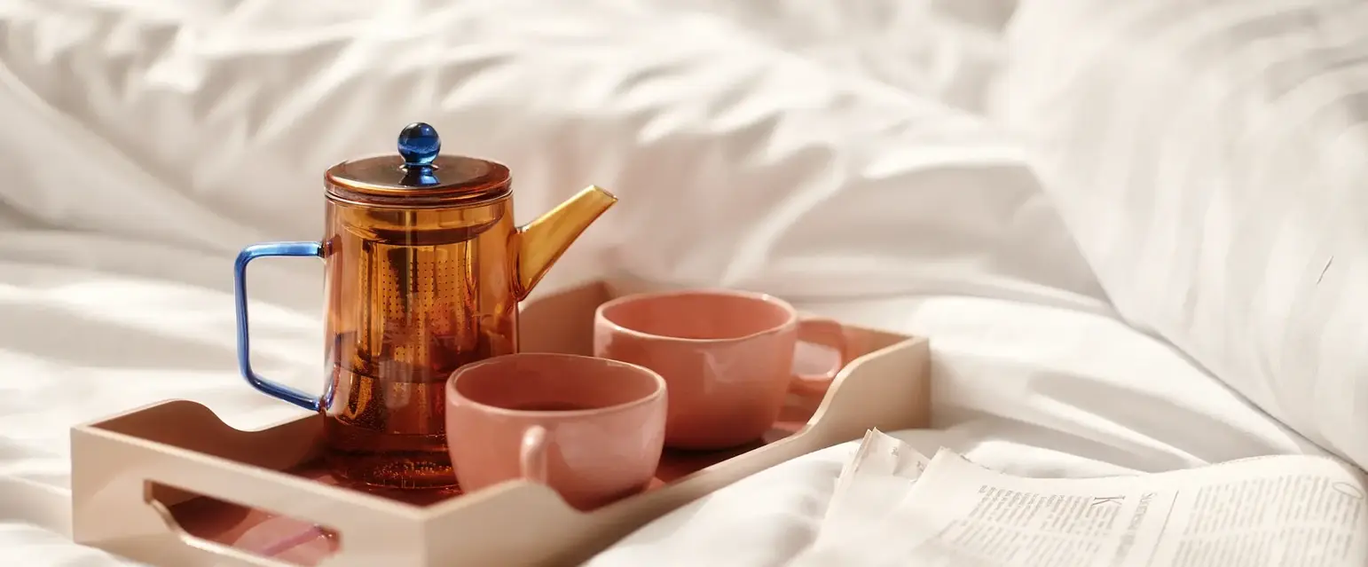 a tray with tea set and cups on a bed