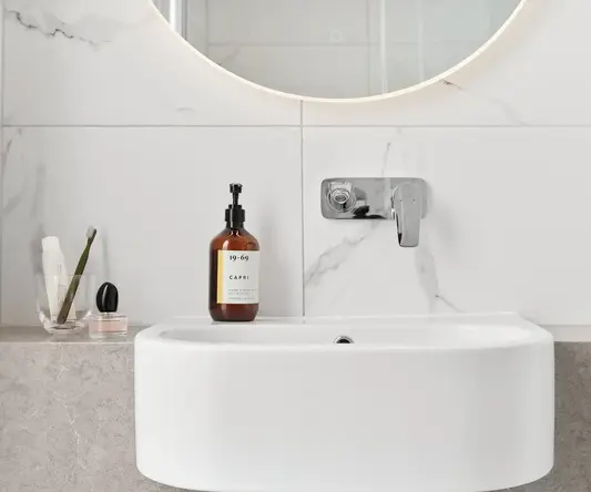 a white sink with a round mirror and a bottle of liquid on it