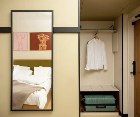 a mirror and a bed with a white shirt and a suitcase