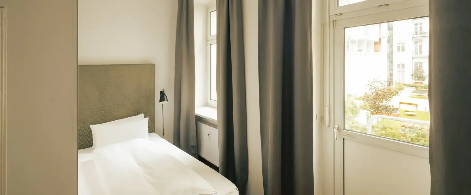 a bed with white sheets and a lamp in a room with windows
