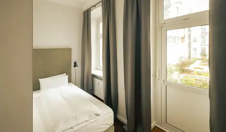 a bed with white sheets and a lamp in a room with windows