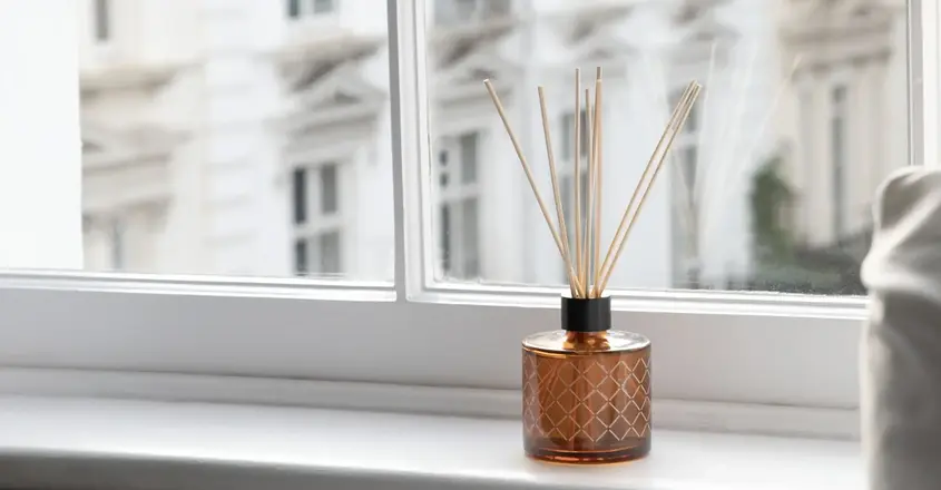 a glass bottle with sticks in it sitting on a window sill