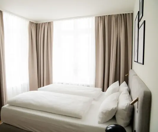 a bed with white sheets and pillows in a room with curtains