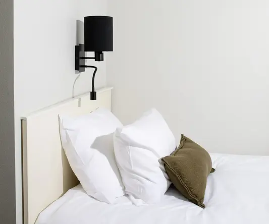 a bed with pillows and a lamp on the wall