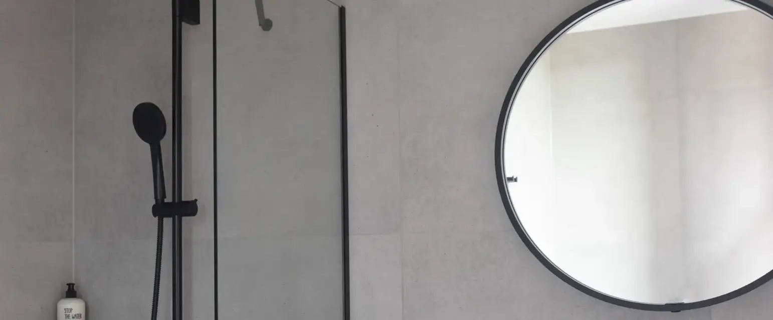 a bathroom with a shower and a round mirror