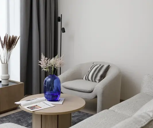 a room with a blue vase on a round table and a grey chair