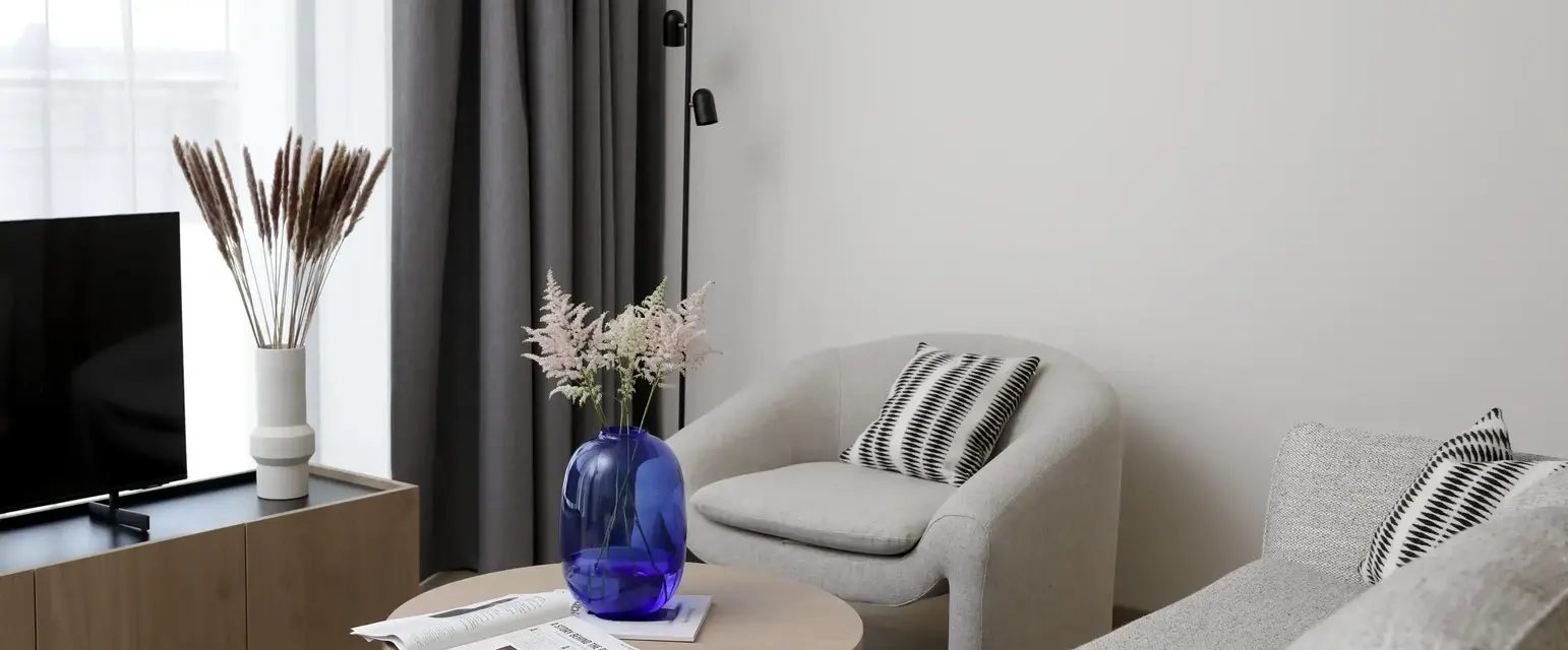 a room with a blue vase on a round table and a grey chair