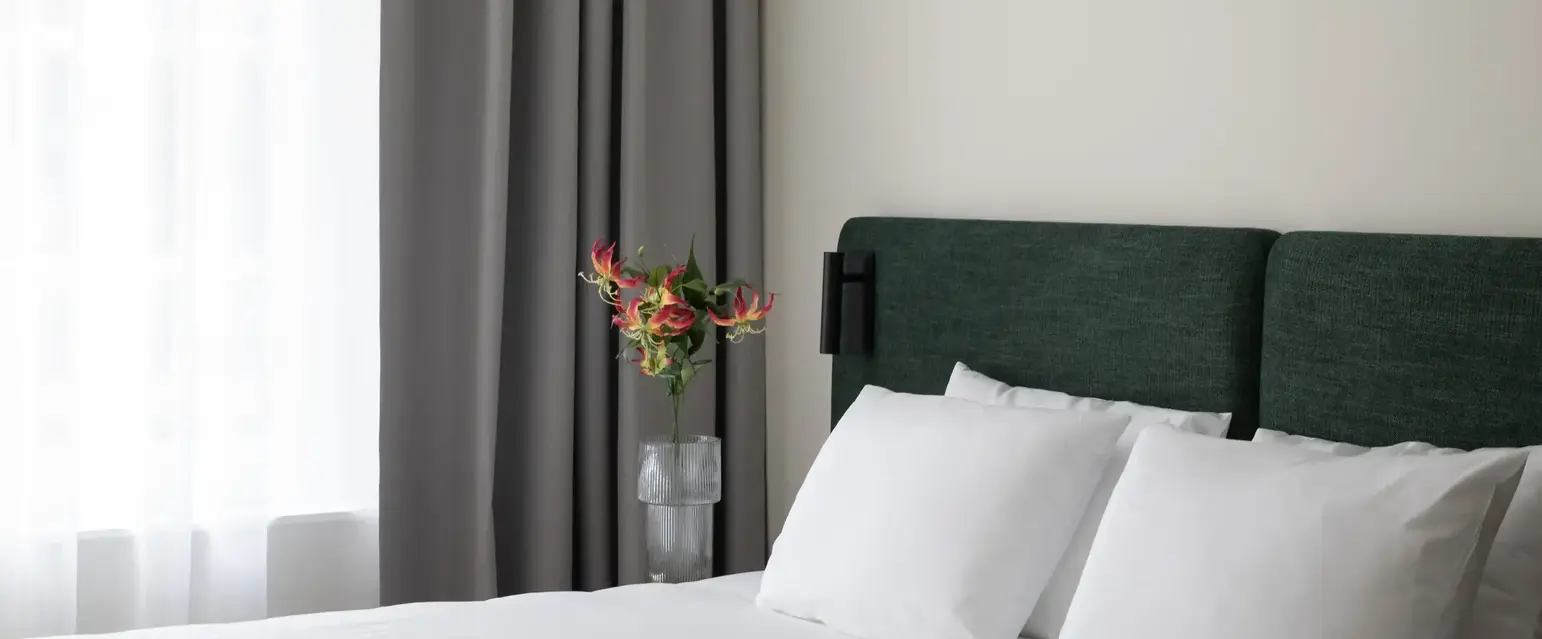 a bed with white sheets and a vase of flowers