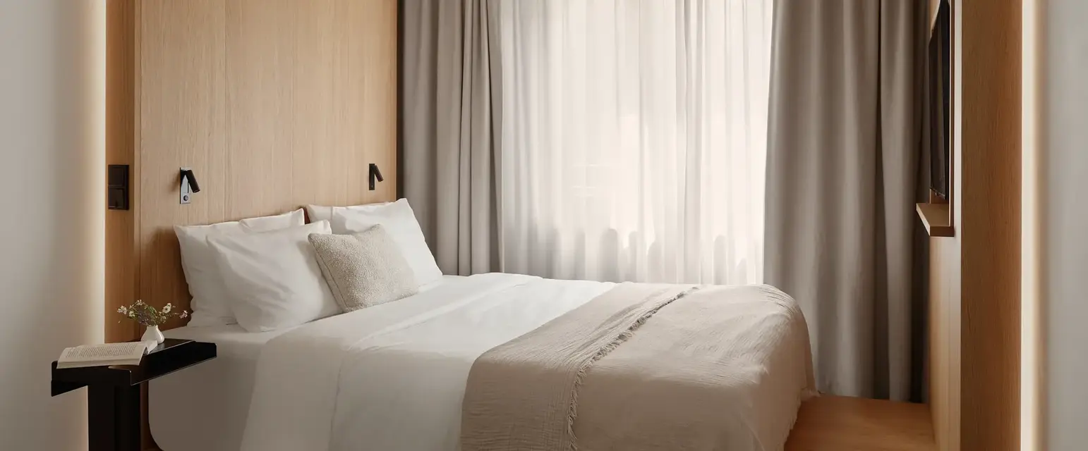 a bed with a white blanket and pillows in a room with a window