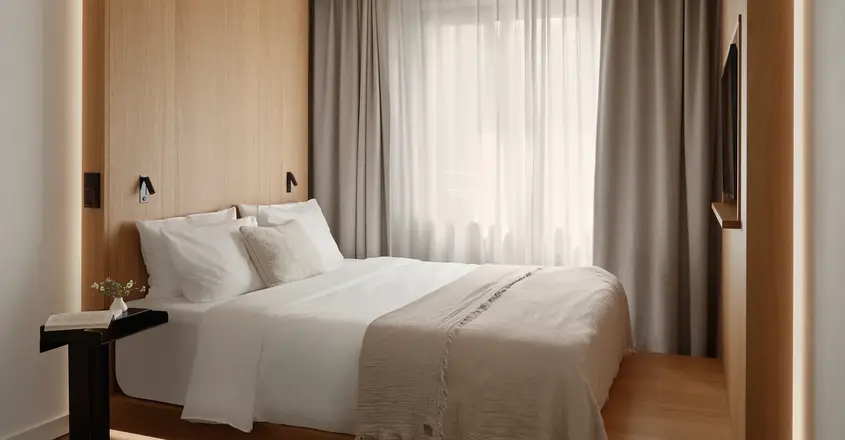a bed with a white blanket and pillows in a room with a window