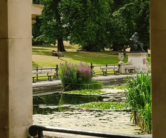 a view through a stone arch of a pond and a statue of a man