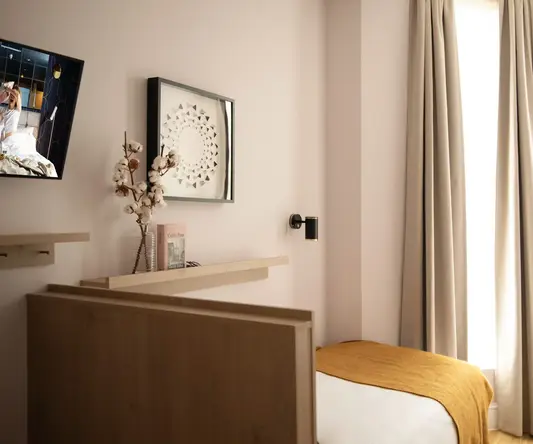 a bed with a yellow blanket and a vase of flowers on a shelf