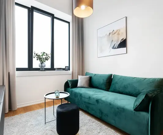 a living room with a green couch and a black stool