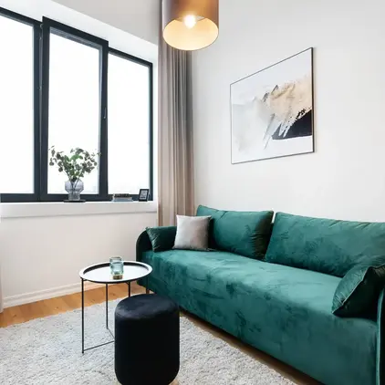 a living room with a green couch and a black stool