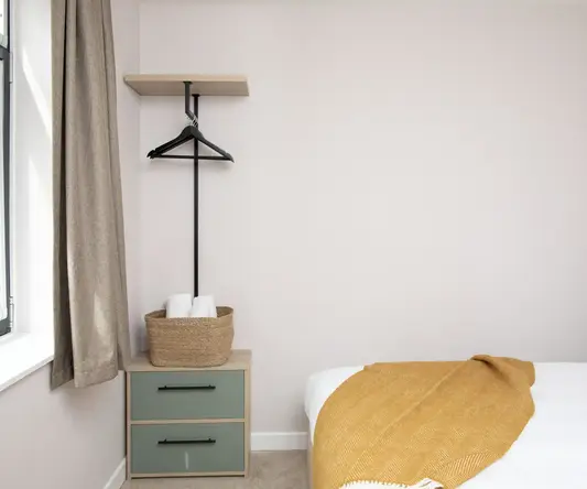 a bed with a yellow blanket and a shelf next to it