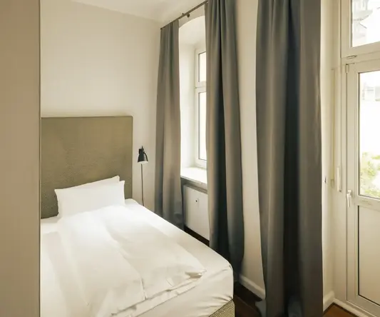 a bed with white sheets and a lamp in a room with windows