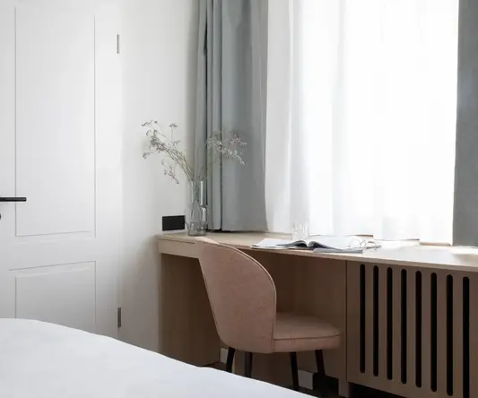 a desk with a chair and a vase of flowers in front of a window
